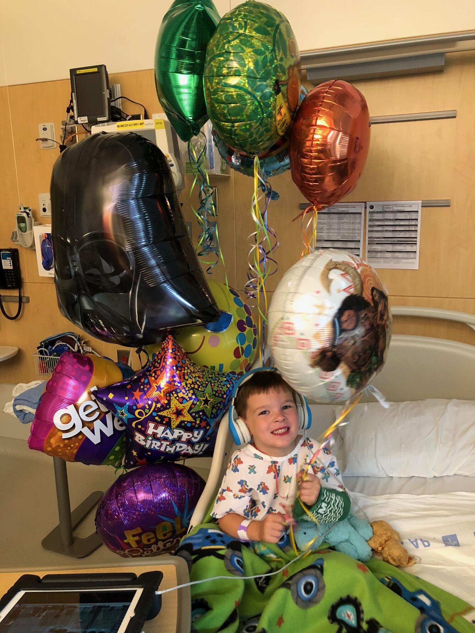Will, a young boy, sits in a hospital bed holding balloons.