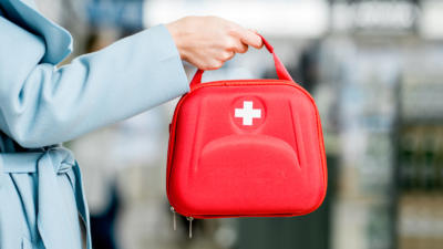 A white person holds a red bag with a medical cross on it.