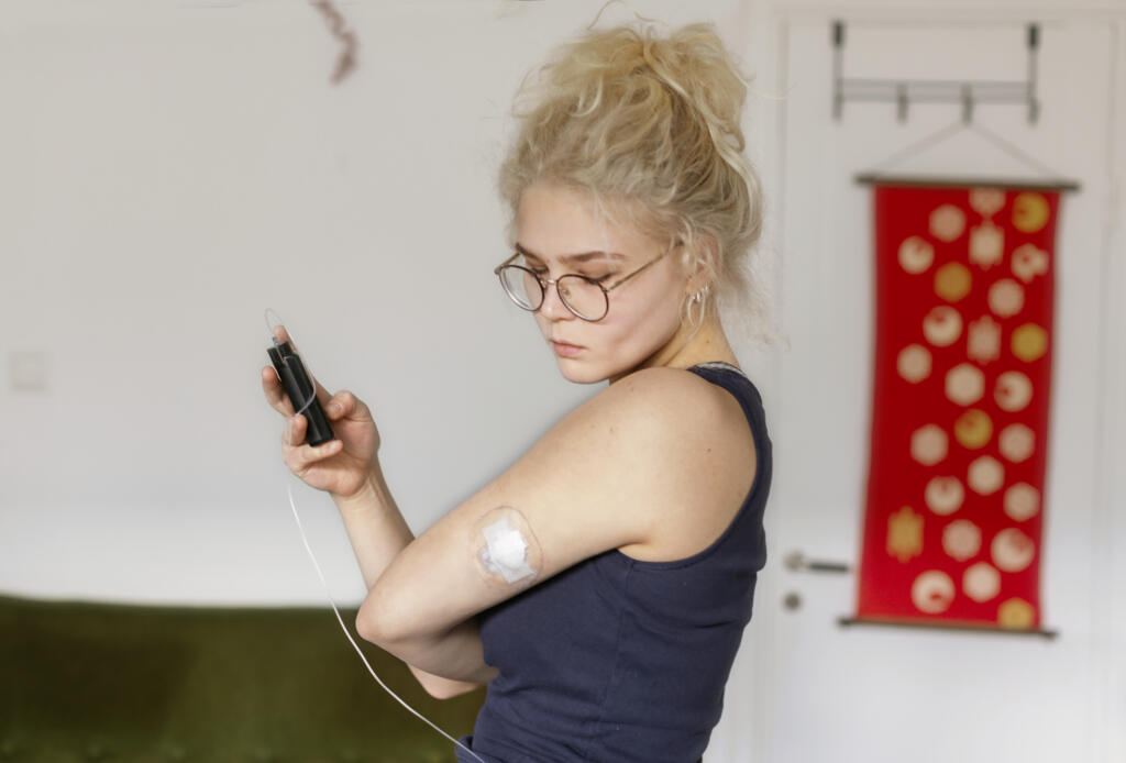 Young woman checks her blood sugar using a continuous glucose monitor