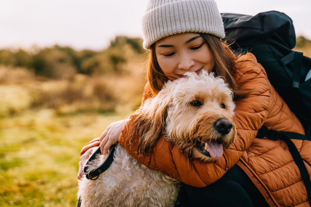 Young woman hugging her dog while hiking in autumn nature. Emotional support and mental health.
