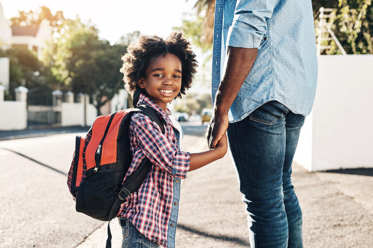 Young boy holding his dad's hand and wearing a backpack goes back to school