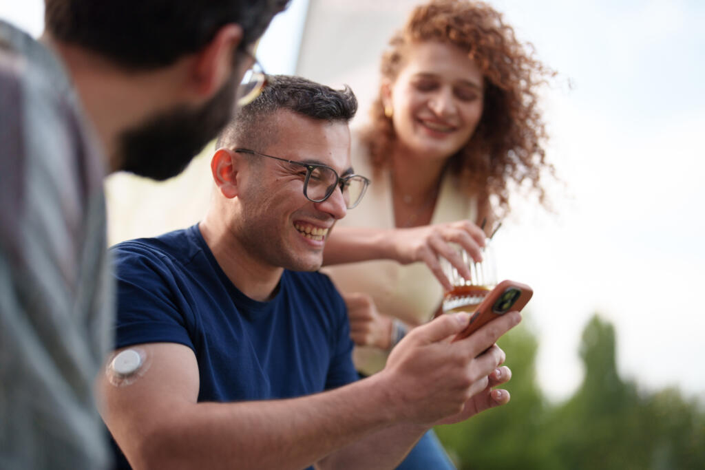 A group of friends enjoying a laid-back afternoon together, filled with laughter, connection, and warmth. One of them, a young man living with Type 1 diabetes, wears a continuous glucose monitoring device on his arm.