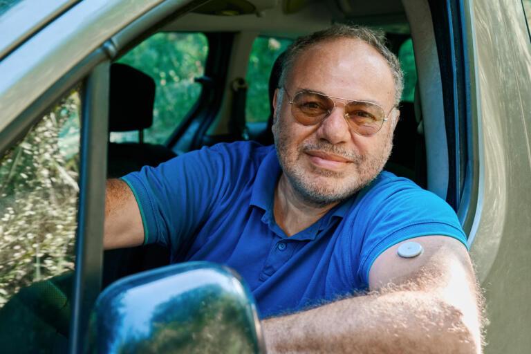 Older man with type 1 diabetes wears a continuous glucose monitor on his arm while driving
