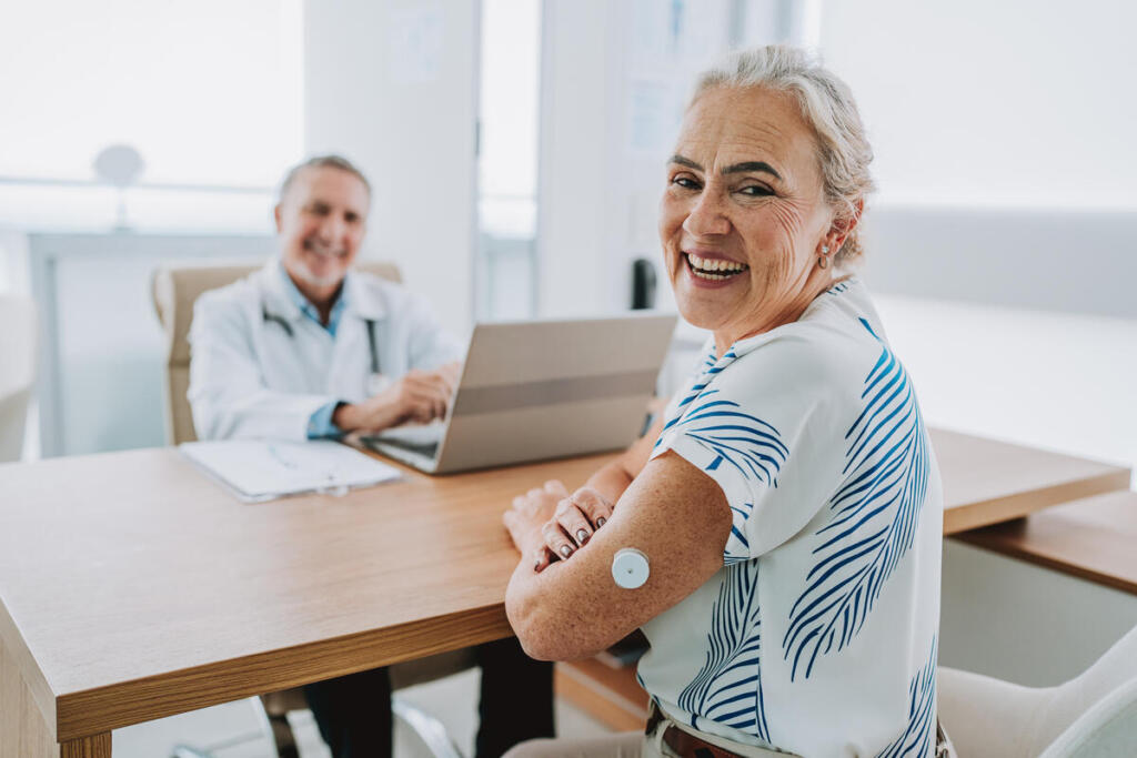 Older woman with type 1 diabetes wears a continuous glucose monitor while speaking with her doctor.