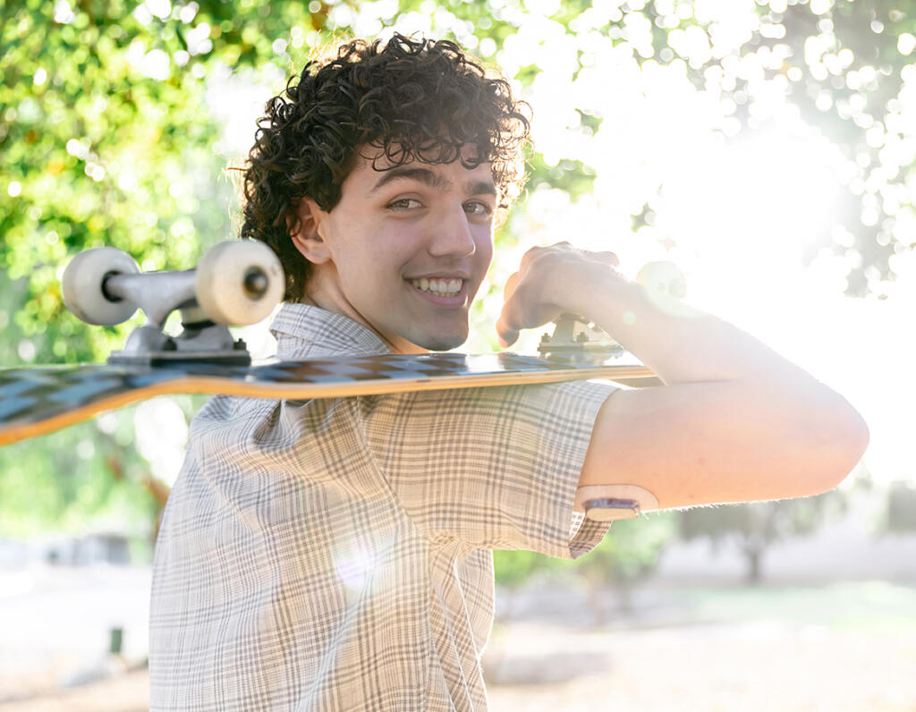 Teenage boy holding a skateboard and wearing a continuous glucose monitor