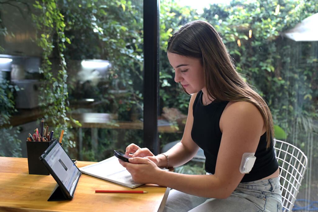 Young woman with type 1 diabetes wears a pod style insulin pump on her arm while working at a computer