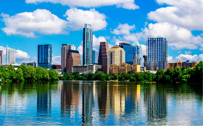Skyscrapers in front of a lake, reflected in the water.