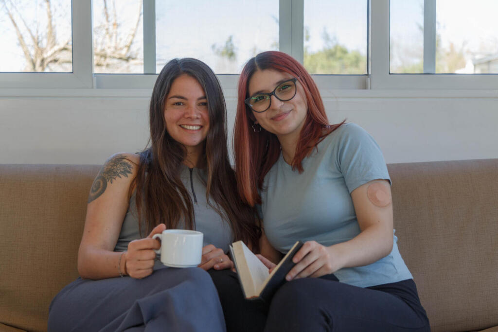 Two female friends, one with type 1 diabetes wearing a continuous glucose monitor on her arm, talk over coffee
