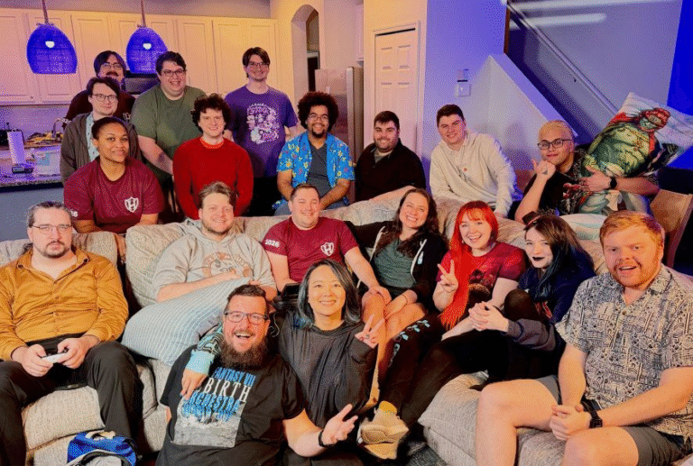 A large group of people sit on a couch while more people stand behind them. All are posing for the camera.
