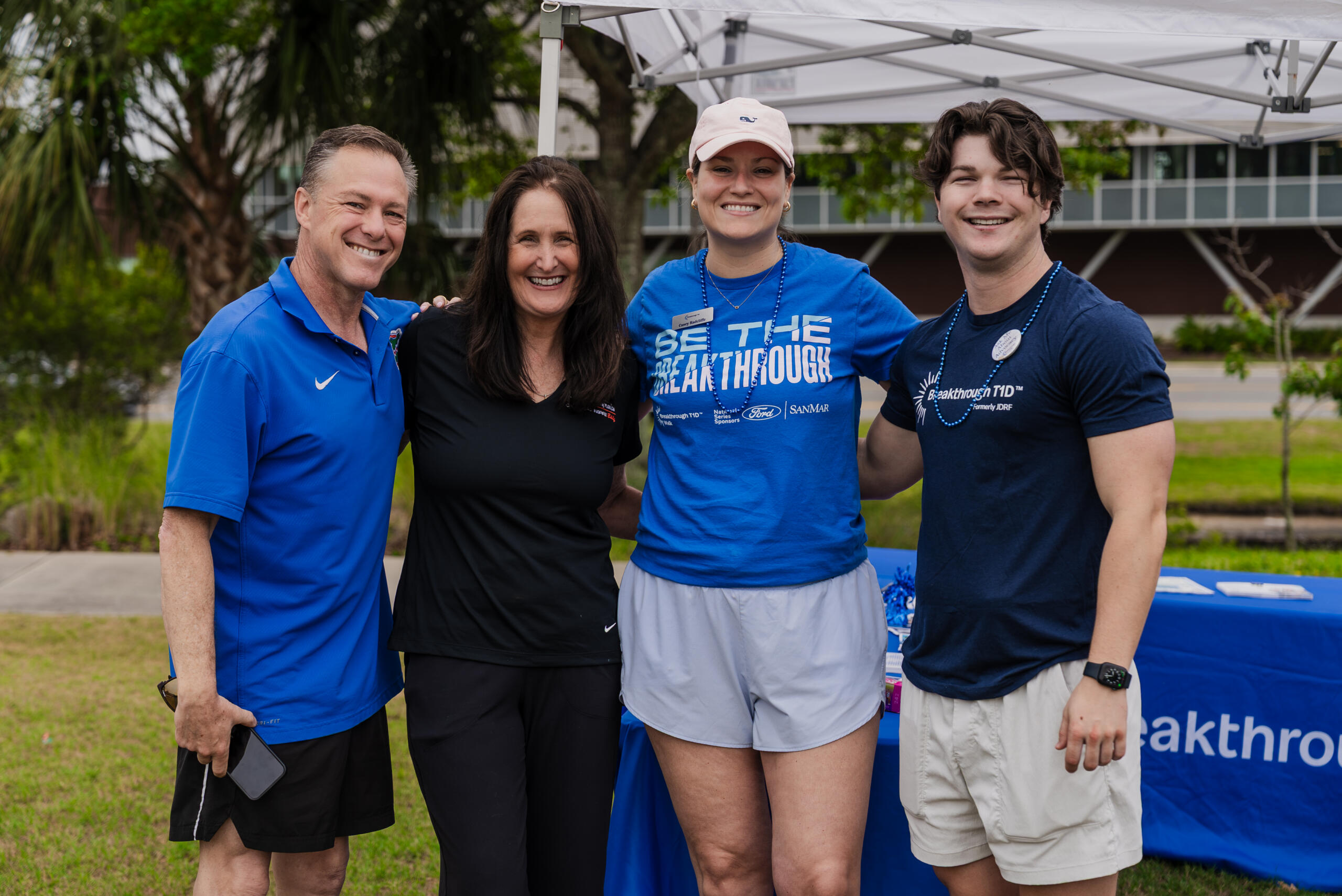 Four white people (two men and two women) smile while standing arm-in-arm. They are wearing athletic clothing and Breakthrough T1D-branded shirts.