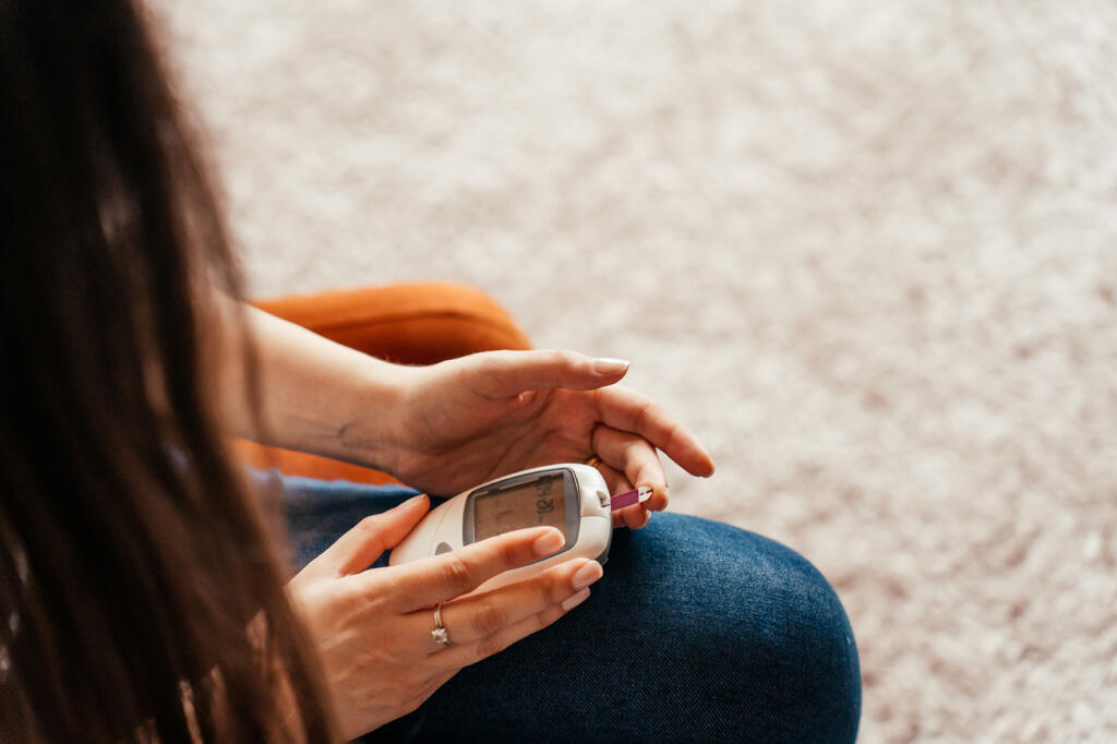 Young woman with type 1 diabetes checks her blood sugar using a glucometer.