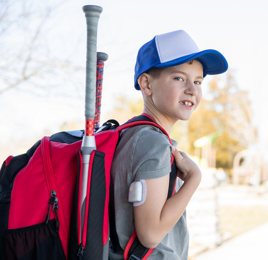 School-aged boy wearing an Omnipod insulin pump and carrying a backpack into school
