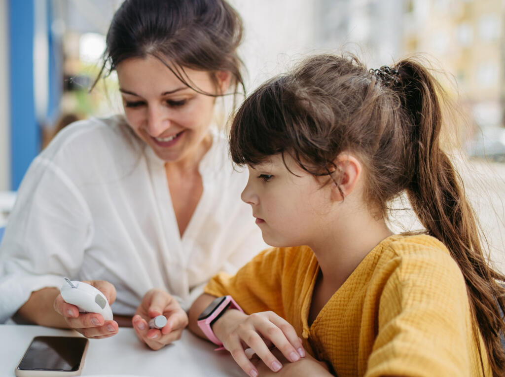 Teacher assists her student with type 1 diabetes in checking her blood sugar with a glucometer.