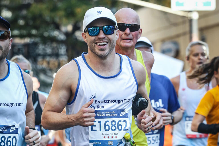 A smiling, bearded white man runs in a marathon crowd while wearing sunglasses and a Breakthrough T1D branded shirt.