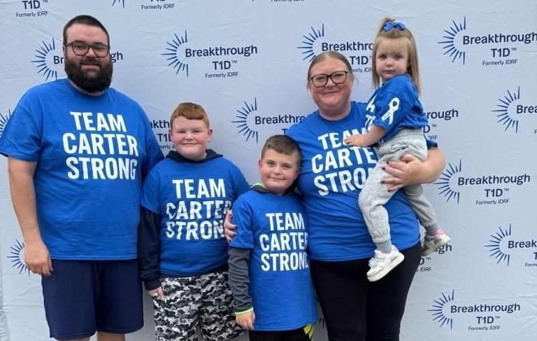 A man, two boys, and a woman holding a girl pose in front of a background reading "Breakthrough T1D."