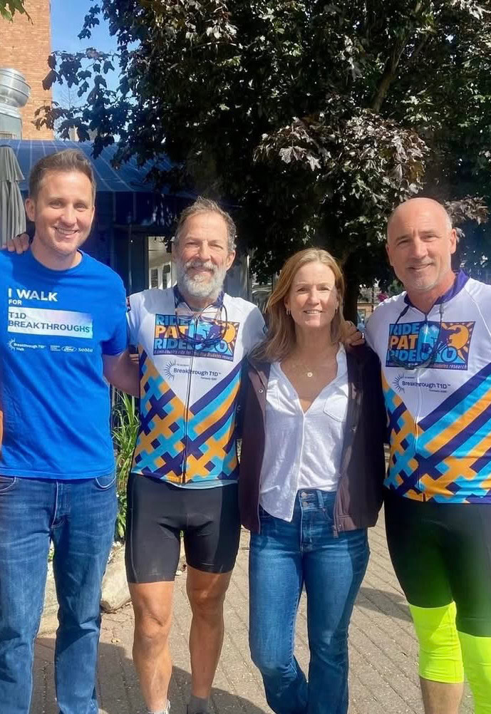 Two white men wearing matching cycling jerseys reading "Ride Pat Ride" pose for a photo wth a white man and a white woman.
